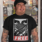 Man wearing Free Palestine JULZ T-shirt featuring narrowed eyes and bandana graphic, with FREE in distressed red letters. Shirt reflects activist spirit, supporting freedom and human rights.