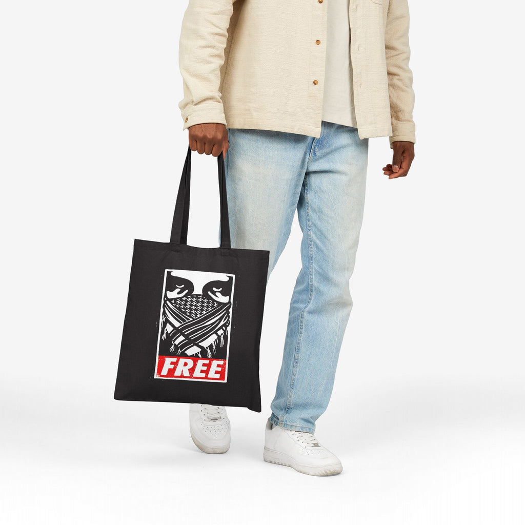Free Palestine JULZ Tote Bag held by a casually dressed person, featuring a stylized graphic of a covered face and bold FREE text, symbolizing activism and support for Palestinian freedom.