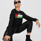 Person squatting wears a Free Palestine Shirt featuring a stylized Palestinian flag graphic. Paired with black faux-leather joggers and ankle boots, embodying activist wear aligned with justice and liberation.