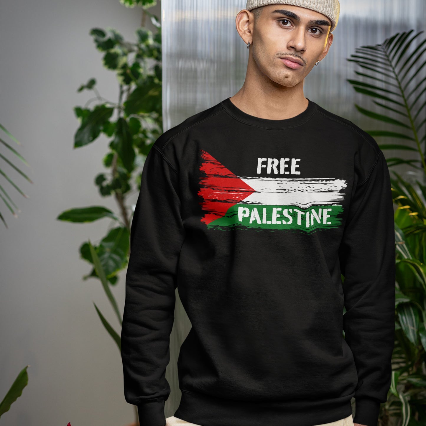 Young man indoors wearing the Free Palestine Shirt, a black crewneck sweatshirt with a distressed Palestinian flag motif and FREE PALESTINE slogan, embodying resistance and solidarity.