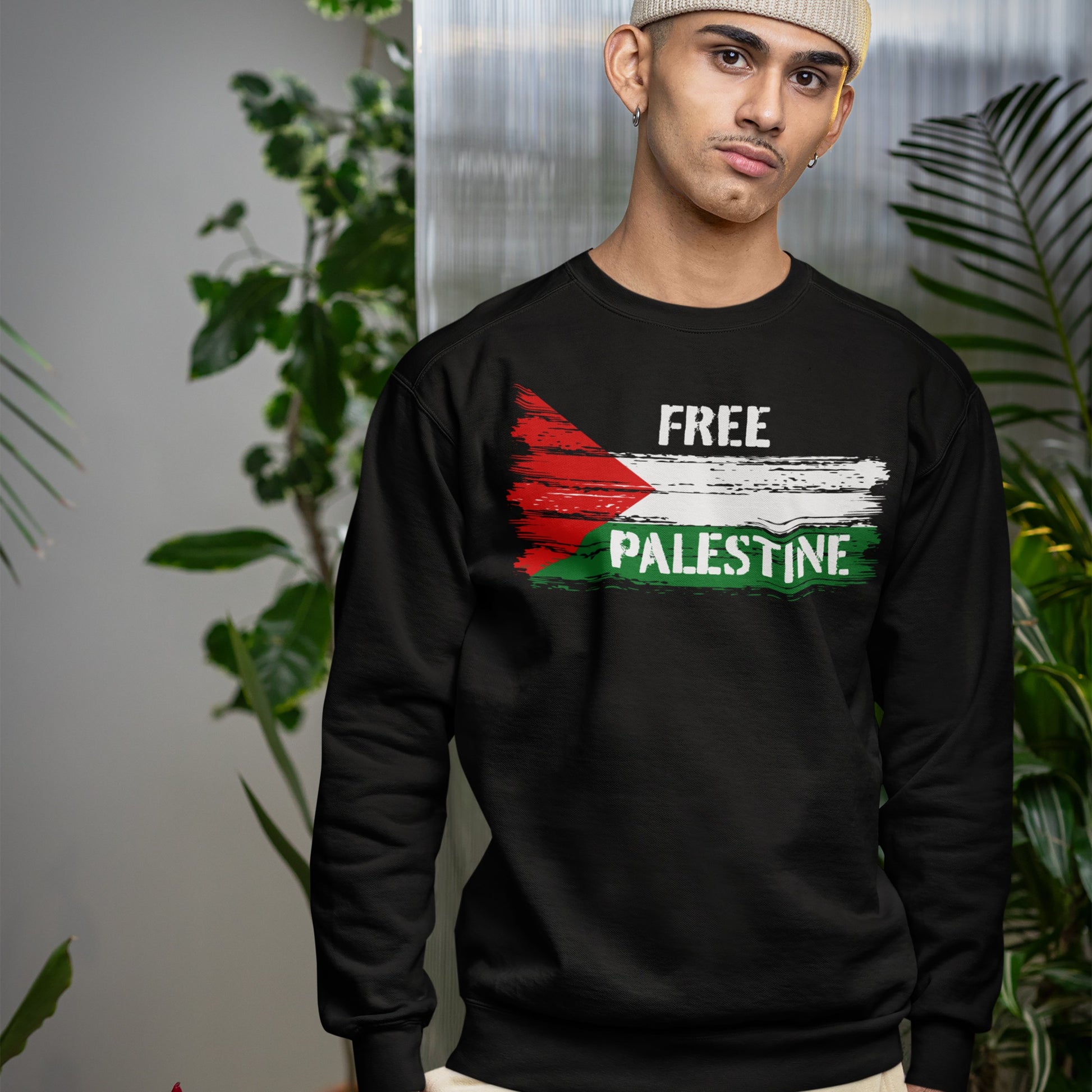 Young man indoors wearing the Free Palestine Shirt, a black crewneck sweatshirt with a distressed Palestinian flag motif and FREE PALESTINE slogan, embodying resistance and solidarity.