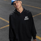 Young person in a black Fuck 'Em All Back Print Shirt with ANTI FASCIST on the chest, embodying a protest-ready stance, styled with a blue cap, septum piercing, and neck tattoo.