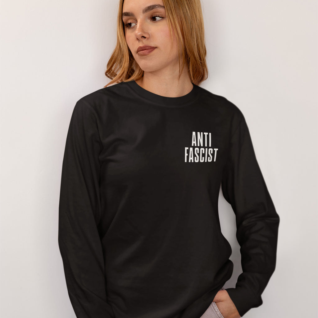 Young woman wearing the Fuck 'Em All Back Print Shirt, featuring a white “ANTI FASCIST” print on the front, embodying resistance and activism. Her right hand is in her pants pocket.