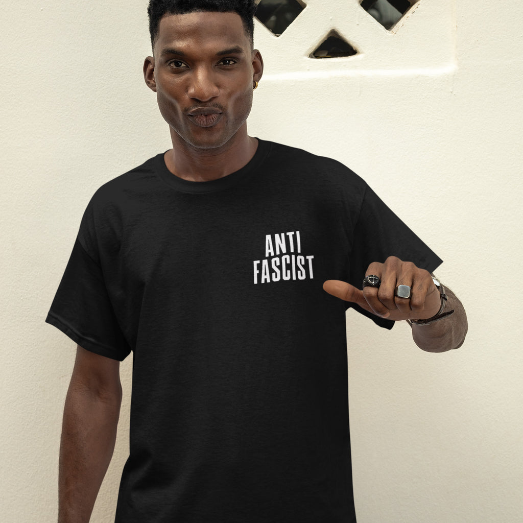 Fuck 'Em All Back Print Shirt: A young man models this unisex protest shirt, featuring “ANTI FASCIST” on the front. He accentuates the message by pointing at the slogan, embodying bold resistance.