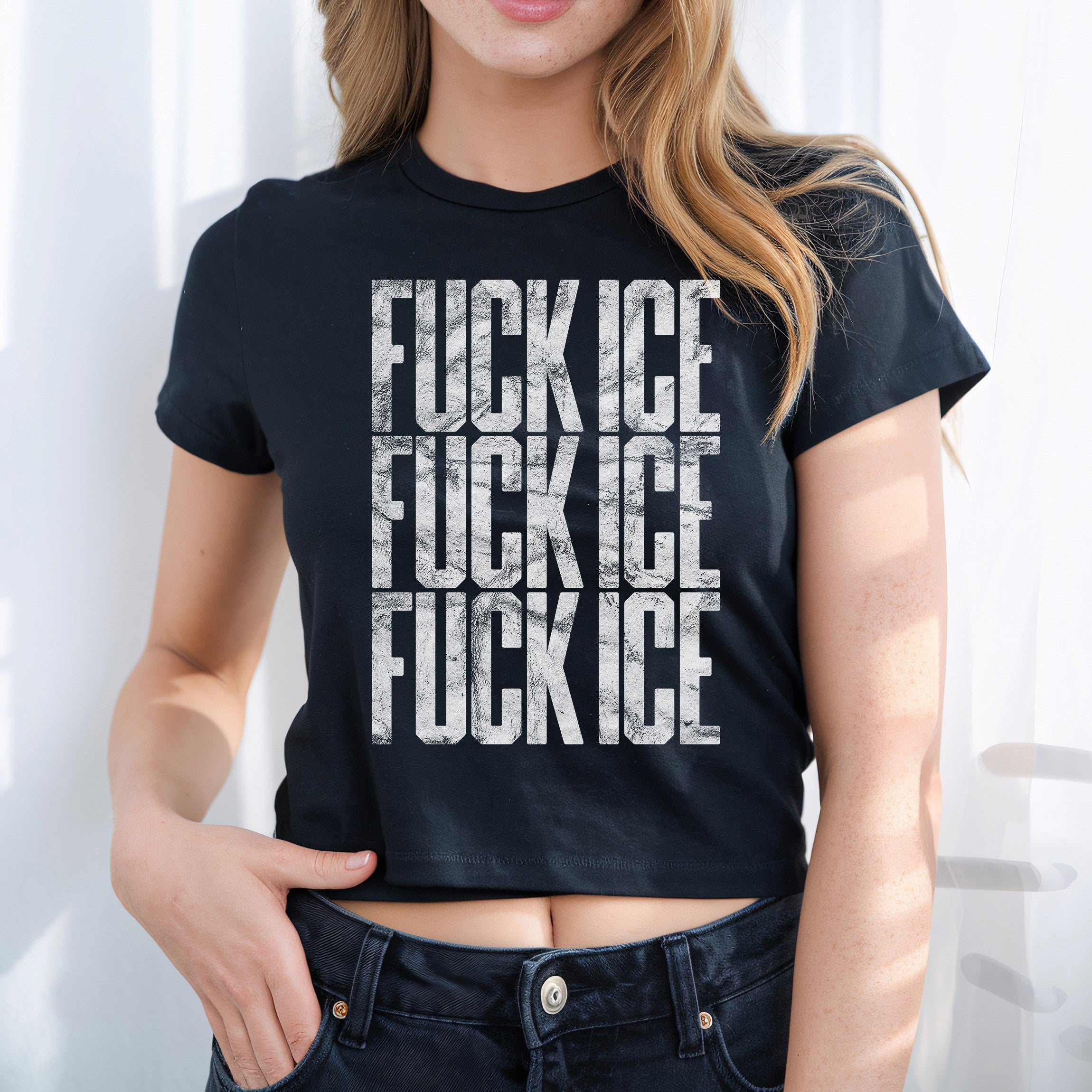 Young woman in a black cropped FUCK ICE baby tee with distressed white lettering, embodying bold activism and street style, hand casually hooked into her dark jeans.