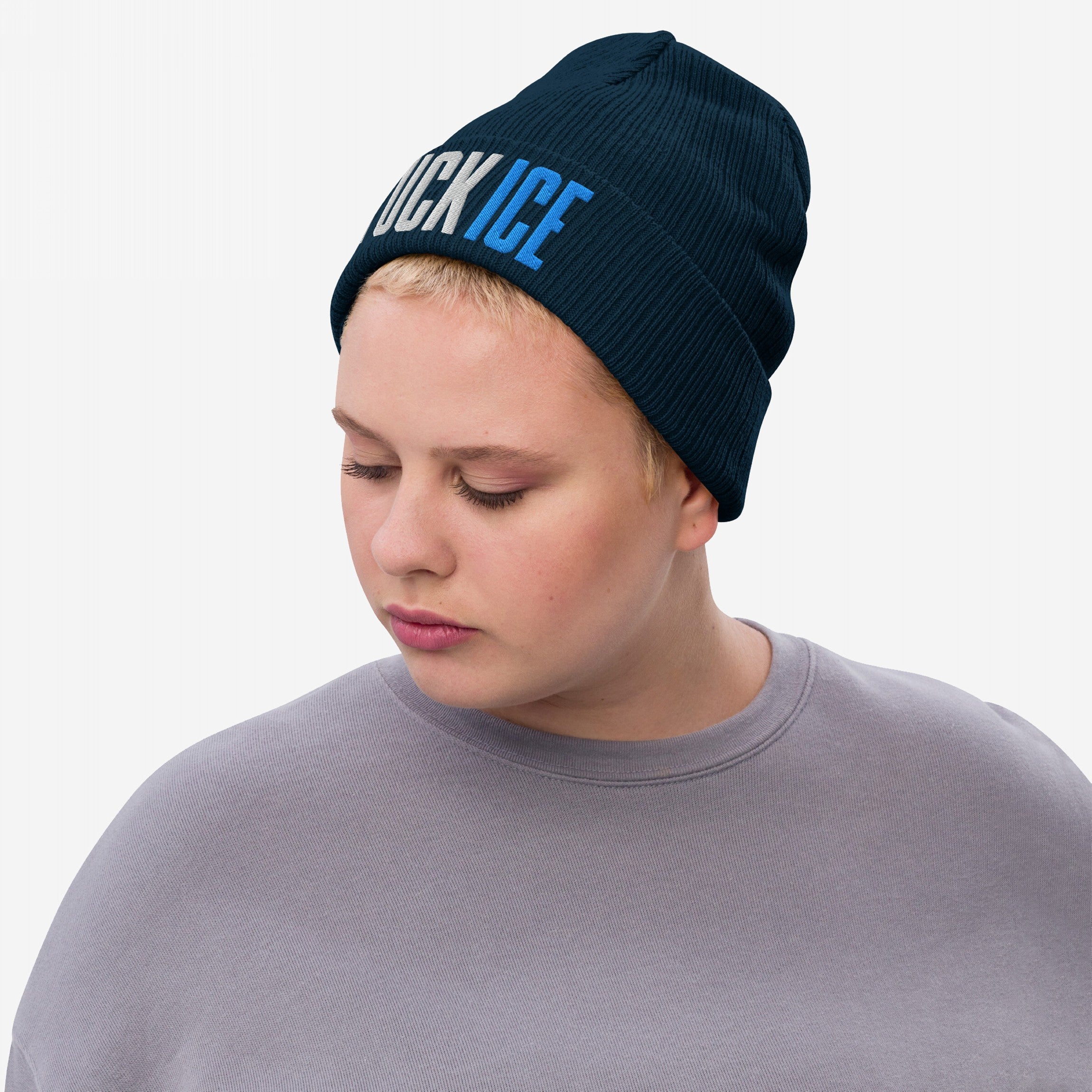 Person wearing a dark navy FUCK ICE knit beanie with bold white and blue 3D embroidery. The beanie is paired with a plain grayish-lavender sweatshirt, highlighting a powerful statement against injustice.