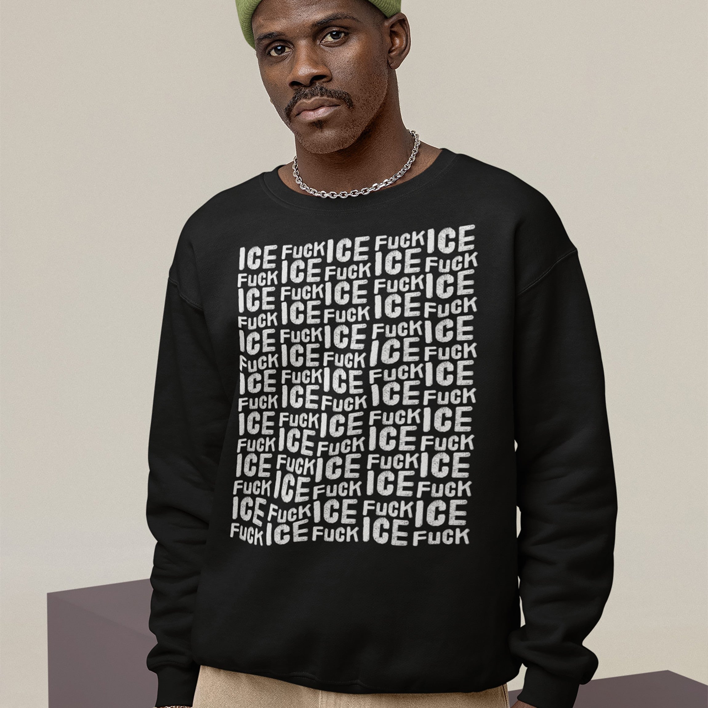 Man in Fuck ICE Pattern Hoodie & Sweatshirt, featuring bold, repeated white text on black. He wears a green beanie and silver chain, embodying anti-fascist, pro-immigrant rights message.