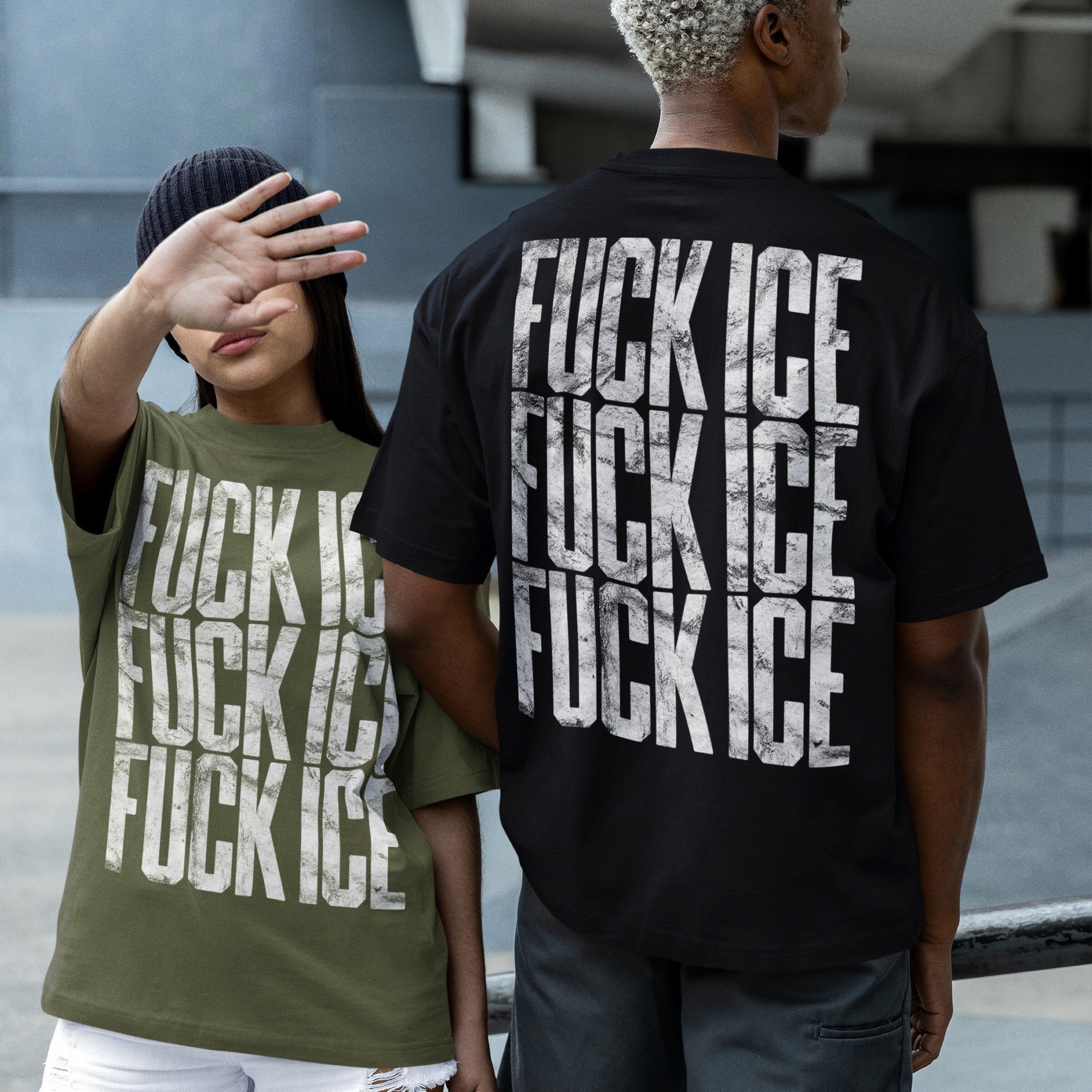 Two people in an urban plaza wear oversized FUCK ICE T-shirts, one olive-green, one black, each with distressed lettering, embodying the bold, activist spirit of the Fuck ICE T-shirt collection.