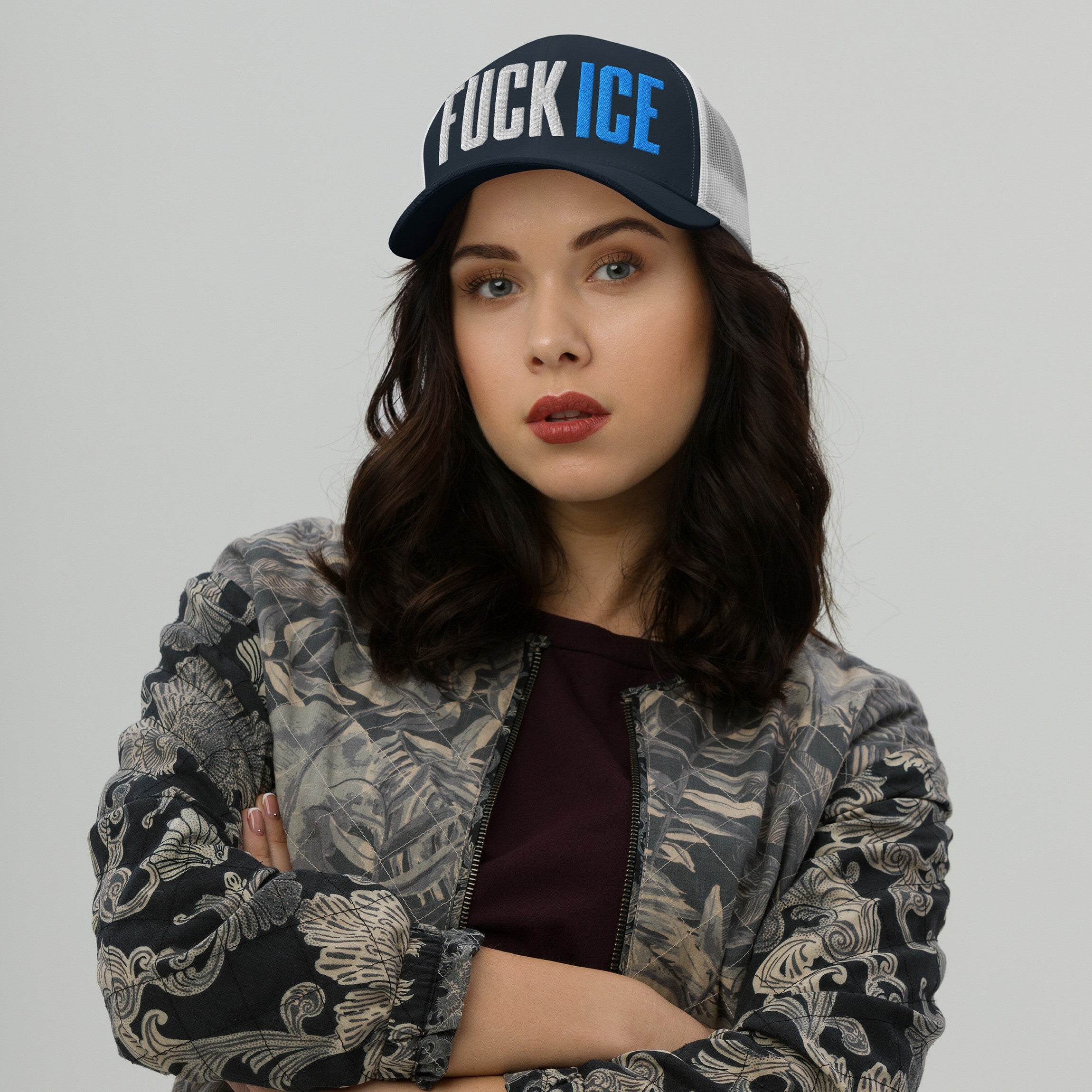 Young woman wearing a FUCK ICE hat with bold 3D embroidery, crossing her arms against a light background. The cap embodies bold activism and personal expression.