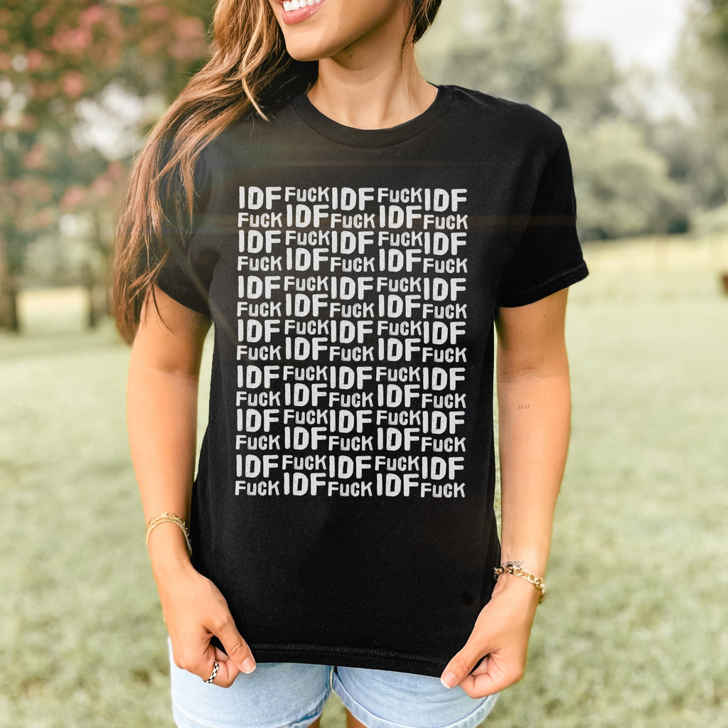 Woman outdoors in denim shorts wearing the Fuck IDF Pattern Women's Baby Tee, featuring a bold text design. The shirt showcases a retro, fitted Y2K style, aligned with anti-war, pro-human rights messaging.