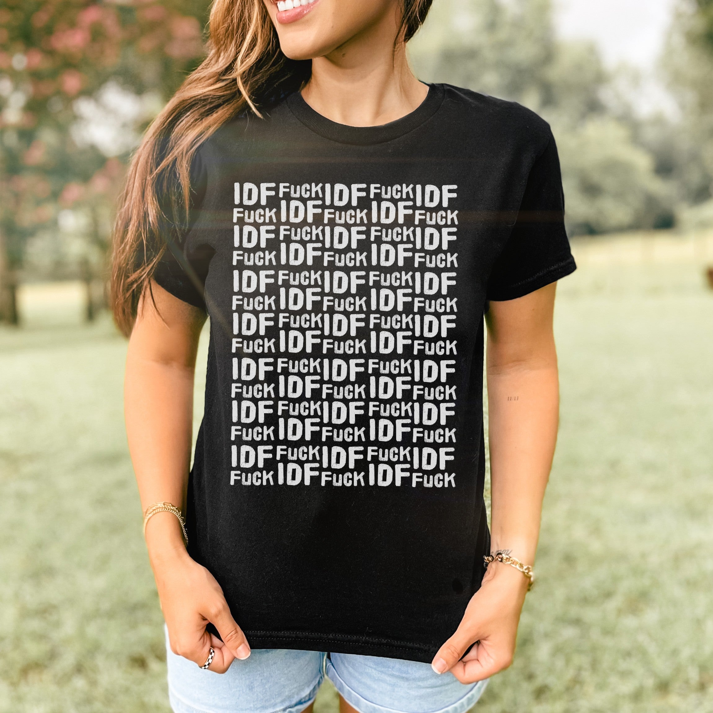 Woman outdoors in denim shorts wearing the Fuck IDF Pattern Women's Baby Tee, featuring a bold text design. The shirt showcases a retro, fitted Y2K style, aligned with anti-war, pro-human rights messaging.