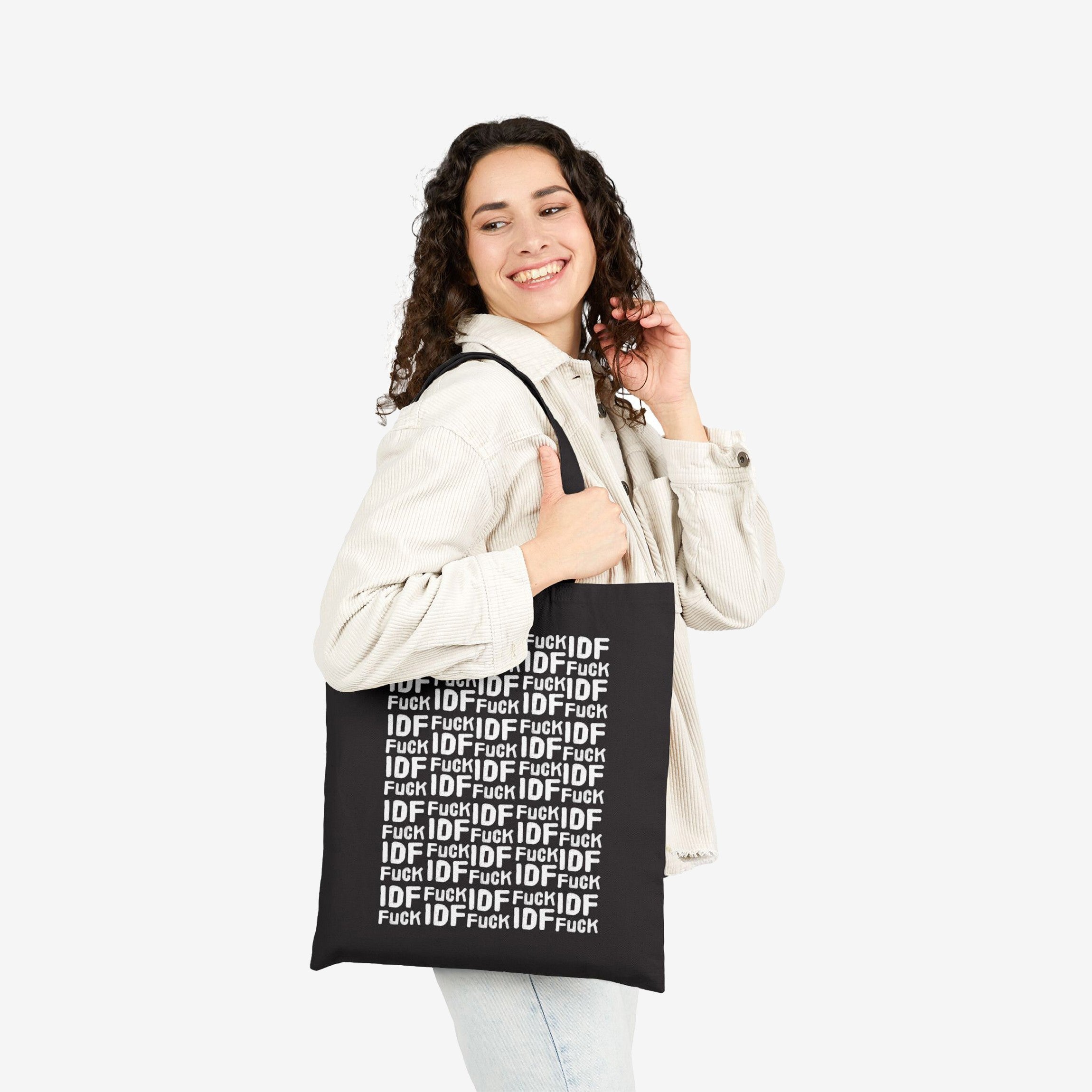 Young woman in a light corduroy jacket carries the Fuck IDF Pattern Tote Bag, showcasing its bold protest message with repeated text. The black canvas tote advocates for Palestinian support and anti-war sentiments.