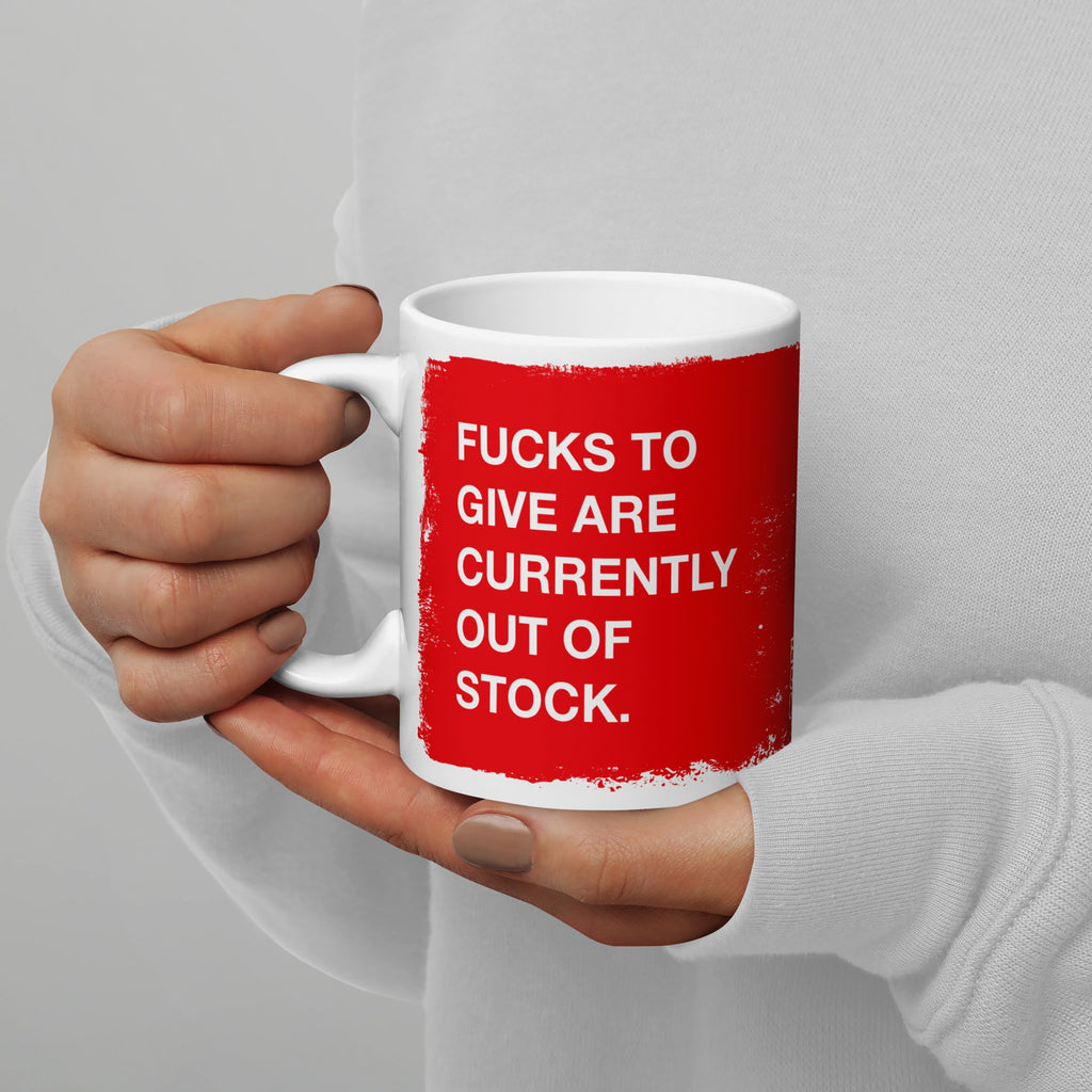 A person holds the Fucks To Give Mug, featuring a bold message FUCKS TO GIVE ARE CURRENTLY OUT OF STOCK in white text on a red square, conveying a humorous, unapologetic vibe.