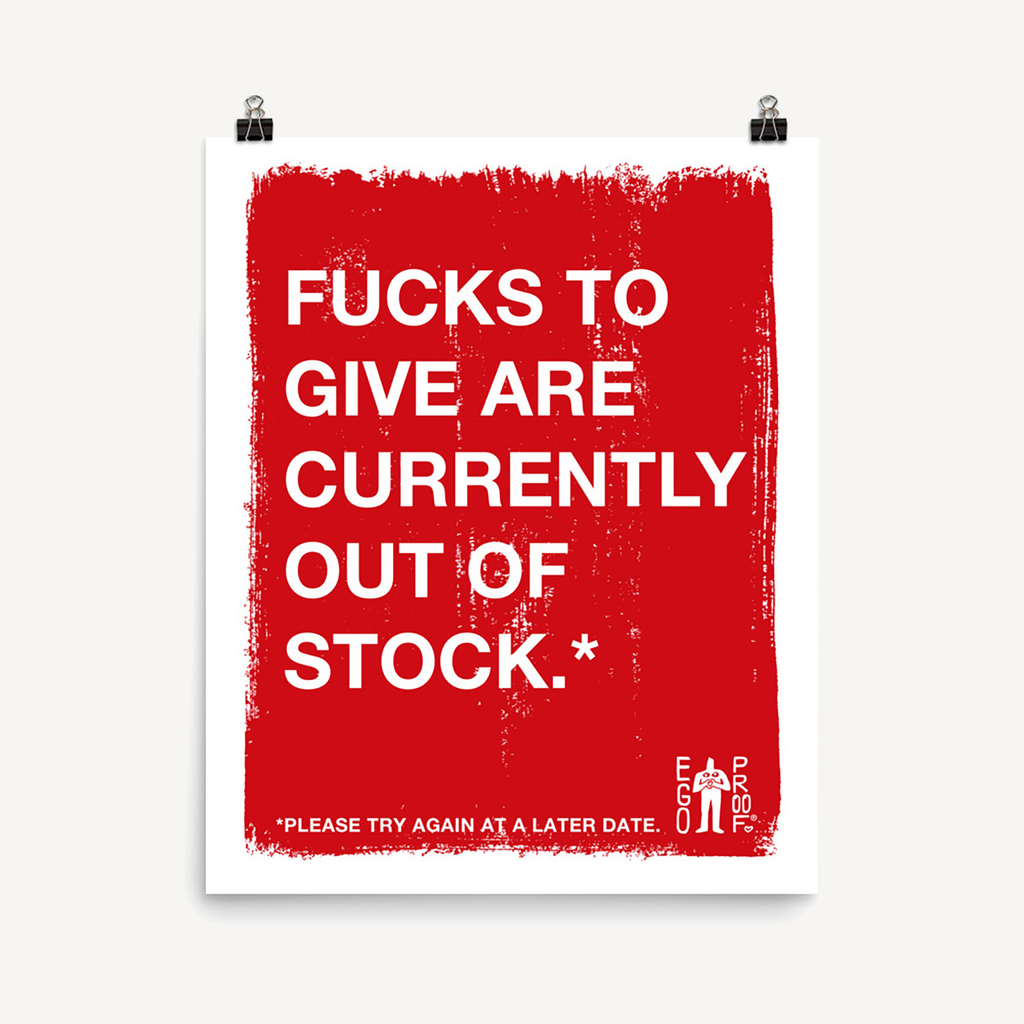 Fucks To Give Giclée Print with bold white text on distressed red background humorously declares emotional exhaustion. Displayed above a light-wood console with black accessories, embodying a modern, playful aesthetic.