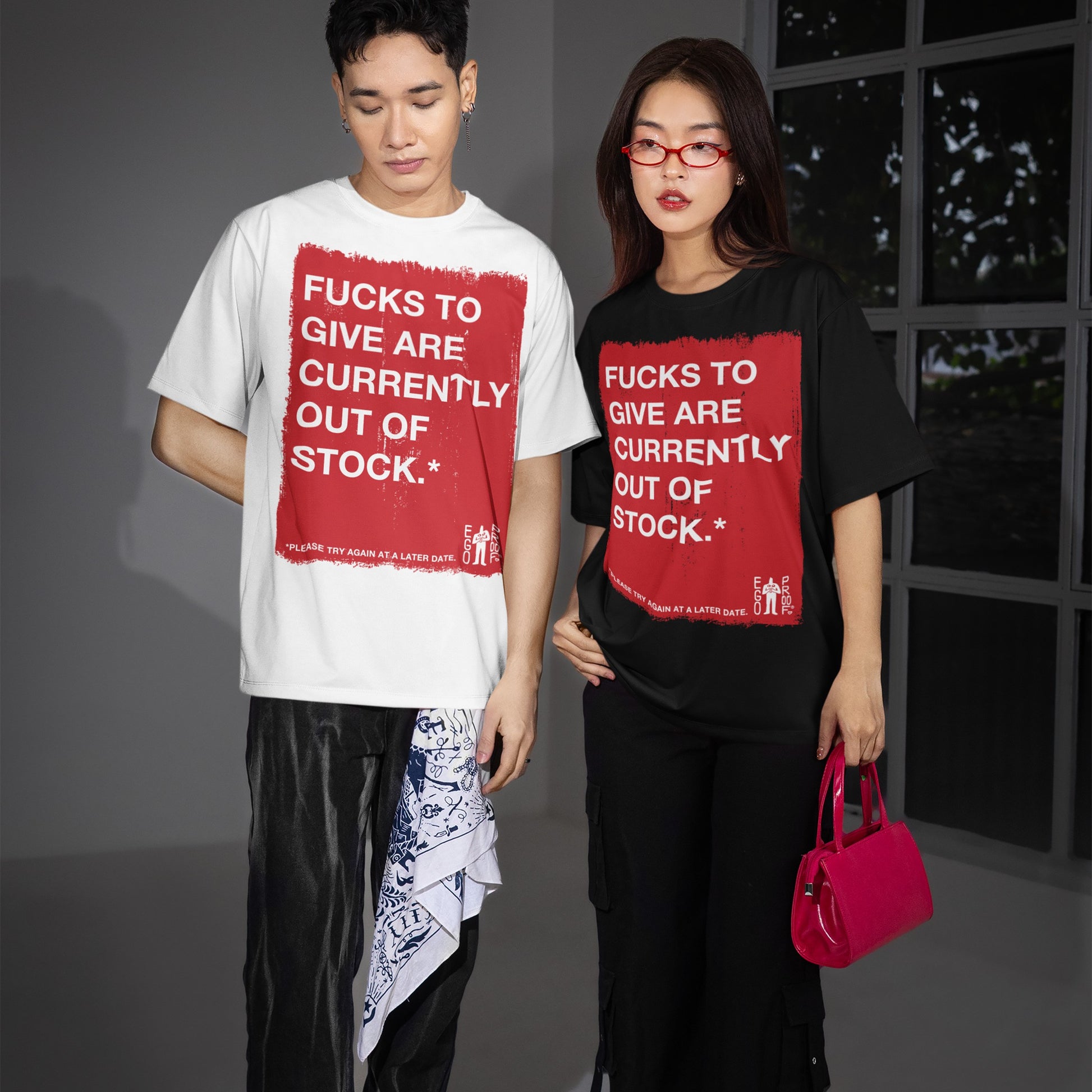 Two young adults wear the Fucks To Give T-shirt, featuring a bold red graphic with a cheeky message, embodying a carefree attitude. One holds a pink handbag; the other sports a bandana.