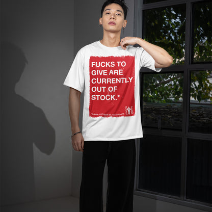 Young man wears a white Fucks To Give T-shirt with bold red square and cheeky message, embodying a carefree, realistic attitude. Casual black pants complement the look indoors by the window.