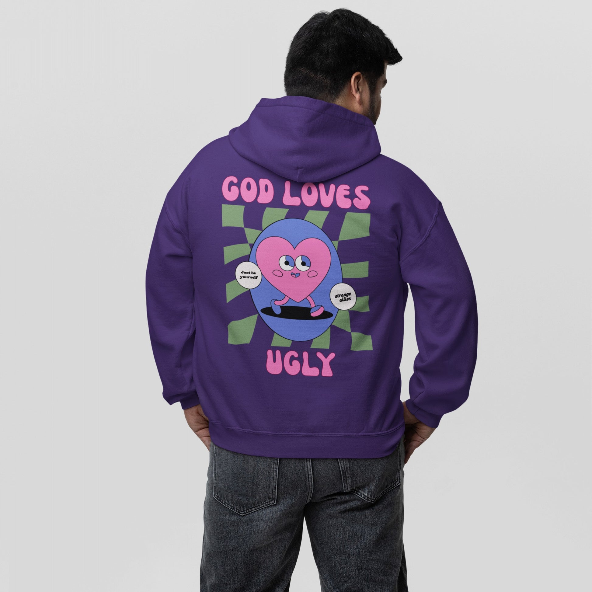 Person wearing God Loves Ugly Hoodie, featuring a bold cartoon graphic of a heart on a skateboard with empowering phrases, embracing uniqueness and defying perfection culture.
