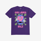 God Loves Ugly T-shirt featuring a cartoonish pink heart character with affirmations, embodying a bold, inclusive message of self-worth, surrounded by vintage comic book style on a purple tee.