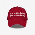 Red Good Day Hat with white embroidered text: it’s a good day for a good day. Perfect for spreading positivity and supporting mental health awareness. Available in various styles.