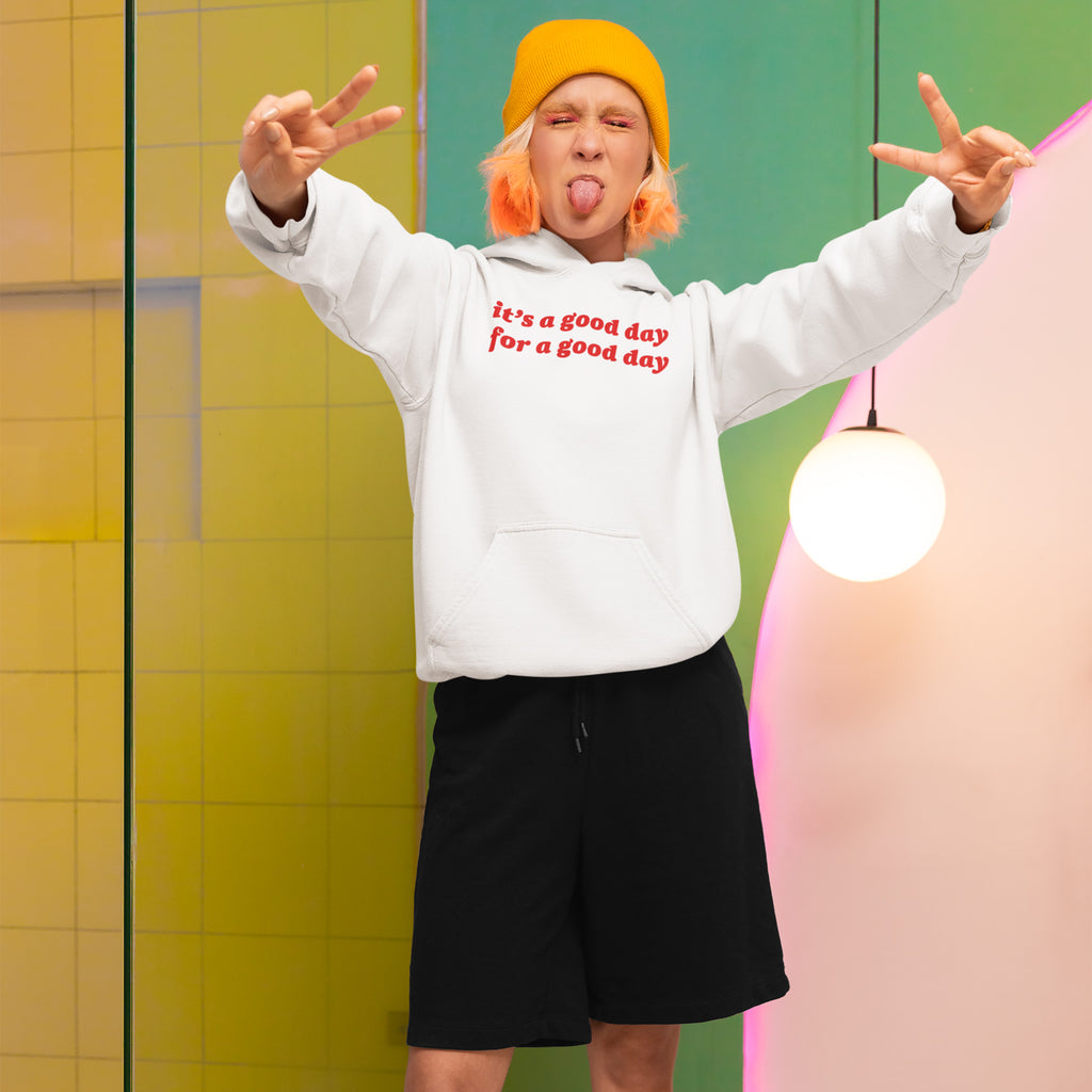 Person playfully poses wearing the Good Day Shirt hoodie, featuring red text for positivity. The vibrant setting enhances its nostalgic charm, perfect for spreading joy and supporting NAMI.