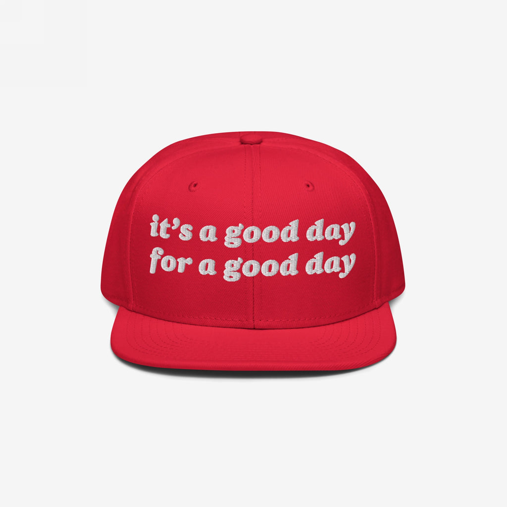 The Good Day Hat features white embroidered text stating it’s a good day for a good day on a red, flat-brim cap, promoting positivity and mental health advocacy with stylish, uplifting flair.