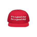 The Good Day Hat features white embroidered text stating it’s a good day for a good day on a red, flat-brim cap, promoting 