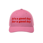 Good Day Hat: A pink trucker-style cap with mesh back, featuring bold red embroidery stating “It’s a good day for a good 