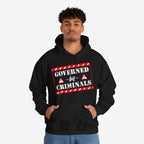 Person wearing Governed By Criminals hoodie featuring a bold red-and-white warning label graphic, symbolizing resistance against political corruption. Ideal for those challenging systems, supporting SPLC.