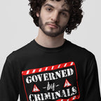 Young man in black long-sleeve Governed By Criminals Shirt featuring bold stencil-style text and red accents, symbolizing rebellion against political corruption and supporting social justice causes.