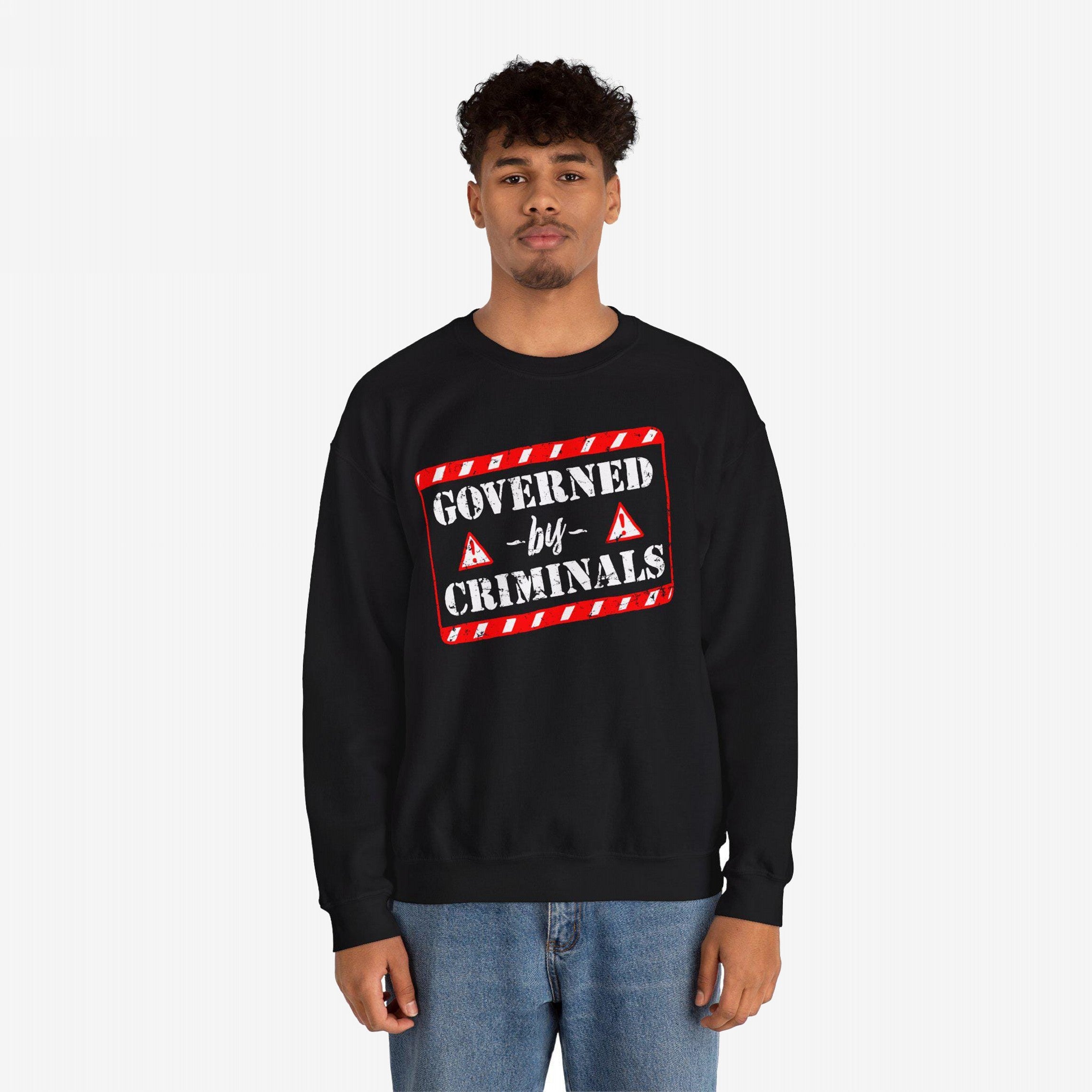 Young man in black Governed By Criminals sweatshirt, featuring a red-and-white warning tape design and stencil-style lettering, paired with medium-wash blue jeans, embodying a rebellious political statement.