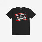Black T-shirt featuring a bold graphic with red-and-white hazard stripes reading “GOVERNED by CRIMINALS,” alongside warning-triangle icons, embodying a rebellious stance against political corruption.