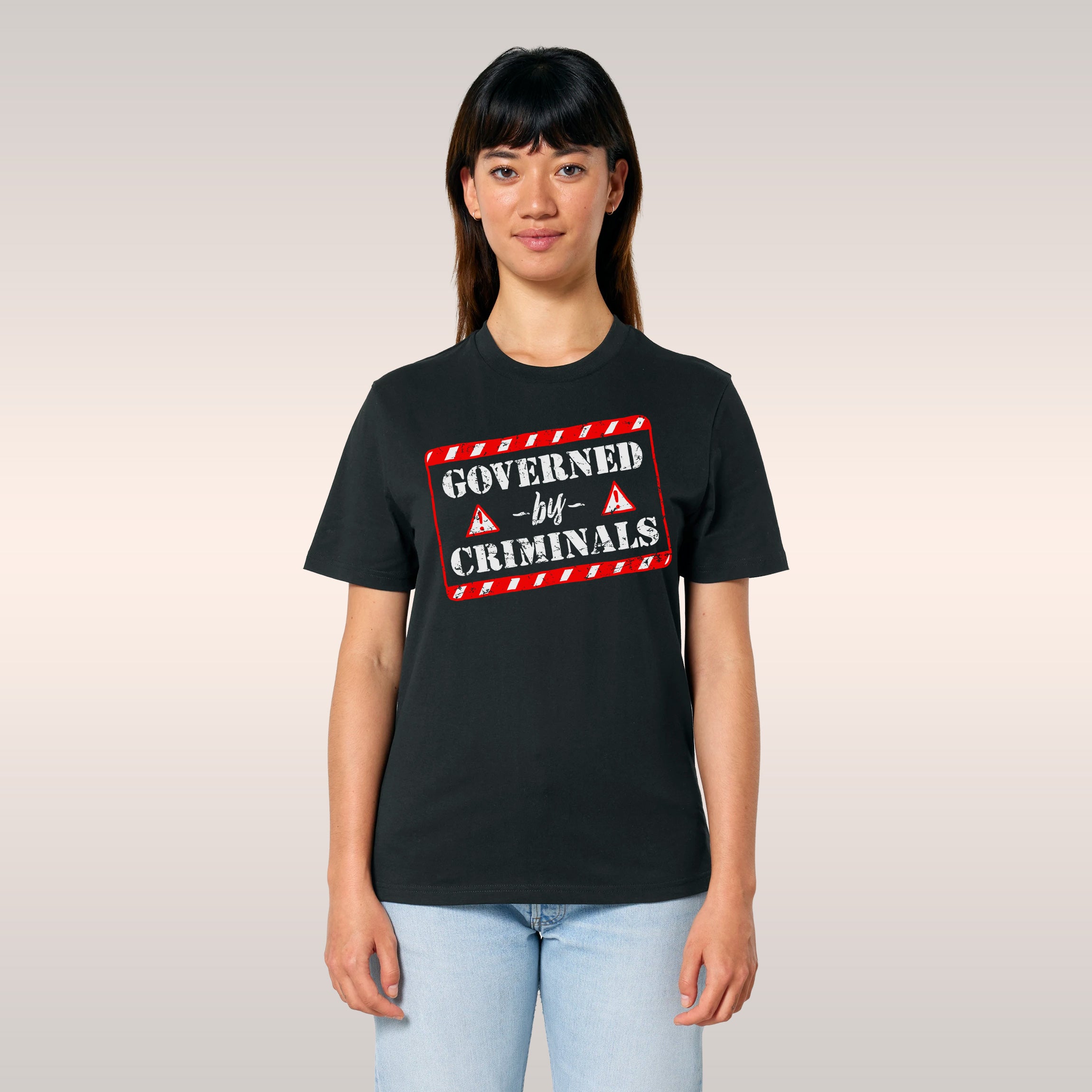 Young man outdoors wearing the Governed By Criminals shirt, featuring a distressed design with a red warning symbol. The shir