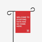 Custom Hate Has No Home Here Garden Flag hanging on a black metal stand, featuring bold white text promoting unity and inclusion. Includes customizable city name space, embodying anti-hate values.
