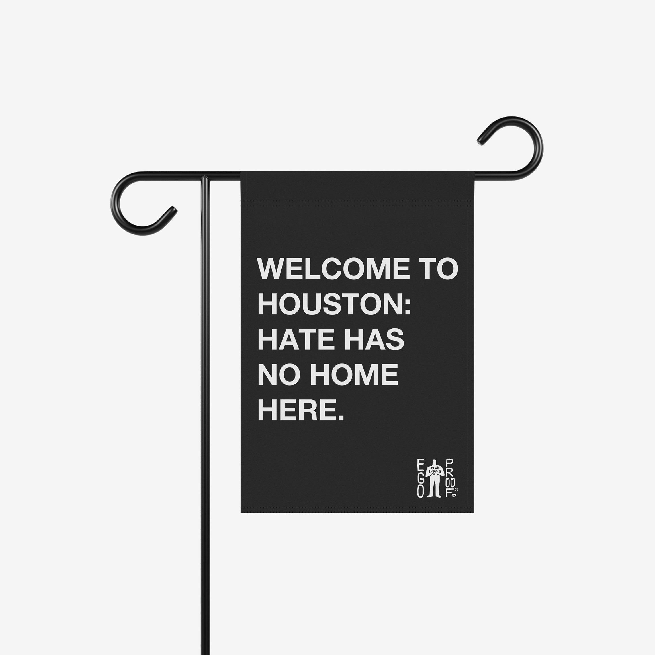 Custom Hate Has No Home Here Garden Flag on a black metal stand, featuring a bold white message welcoming inclusion and unity. A small logo in the corner accentuates this statement of justice and equality.