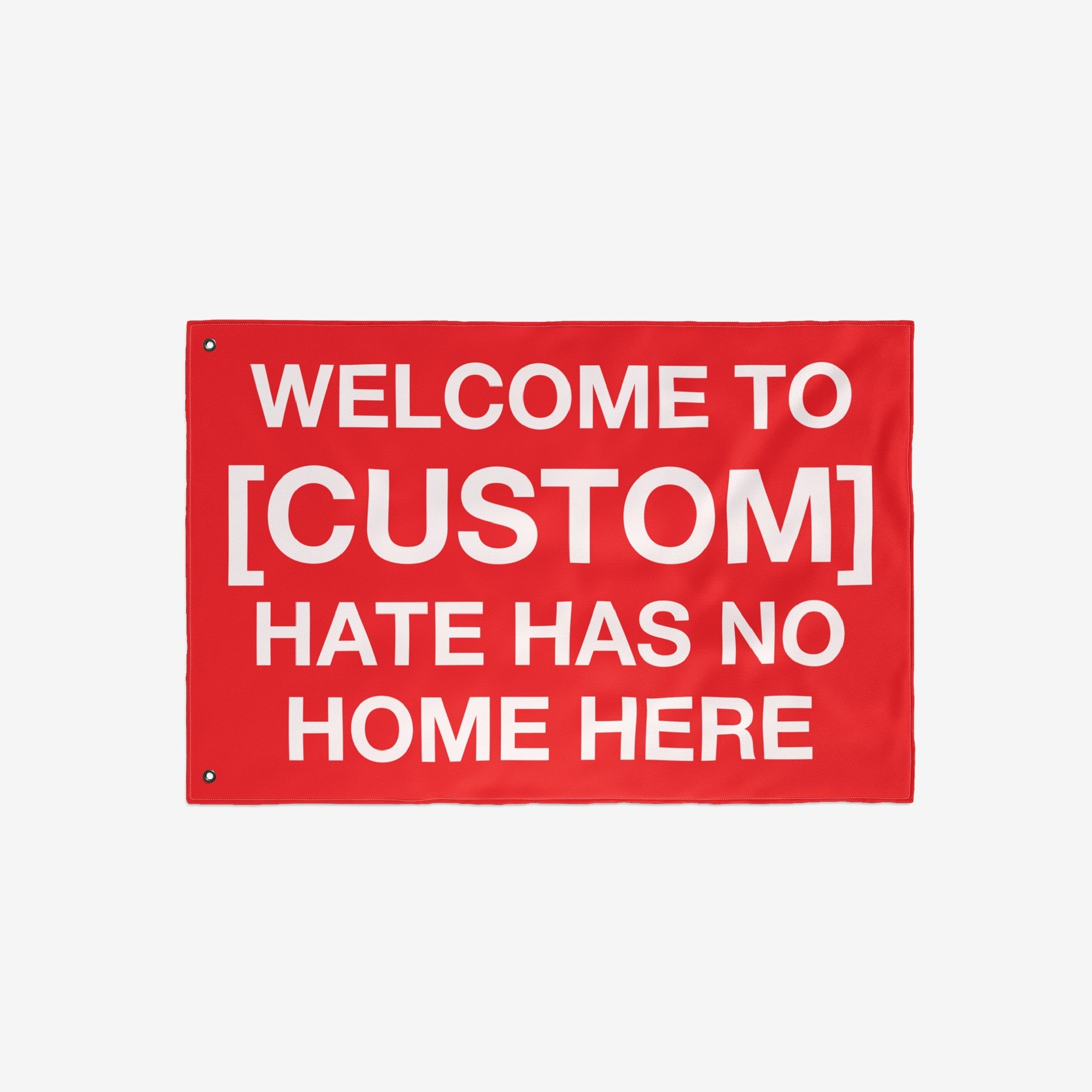 Custom Hate Has No Home Here Flag featuring bold white text on a red background. Includes metal grommets for hanging. Personalize with your city name to promote justice and community resilience.
