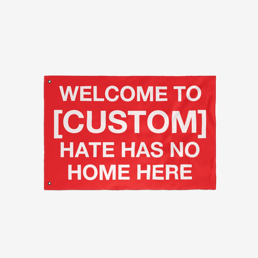 Custom Hate Has No Home Here Flag featuring bold white text on a red background. Includes metal grommets for hanging. Personalize with your city name to promote justice and community resilience.