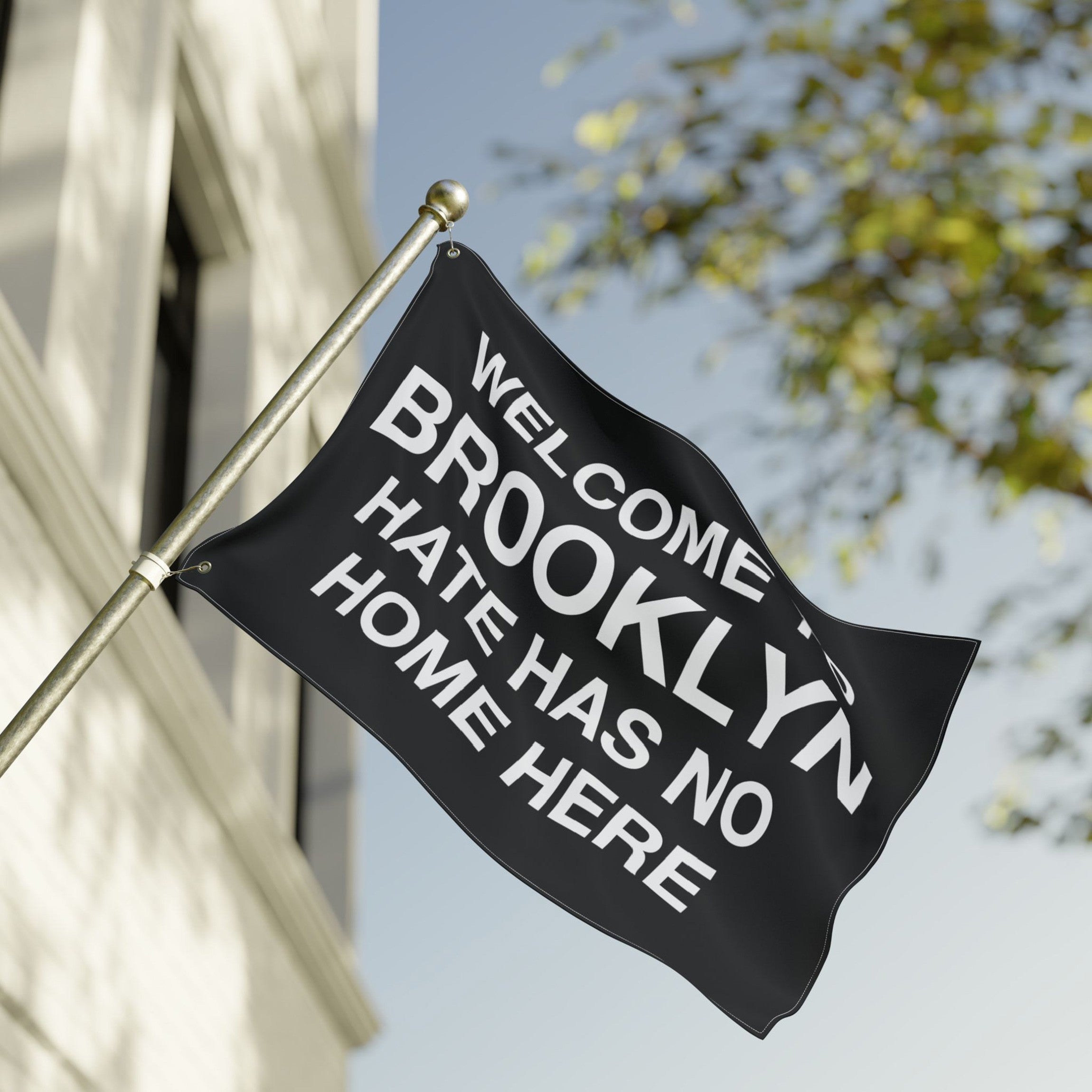 Custom Hate Has No Home Here Flag mounted on a pole outside a building, displaying the message “WELCOME BROOKLYN: HATE HAS NO HOME HERE” in large white letters, symbolizing justice and community resilience.
