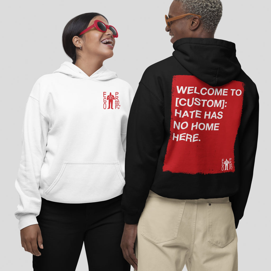 Two people wearing “Custom Hate Has No Home Here Hoodie”; one in a white hoodie with a small “EGO PROD.” logo, the other in a black hoodie featuring a bold, customizable community message on the back.