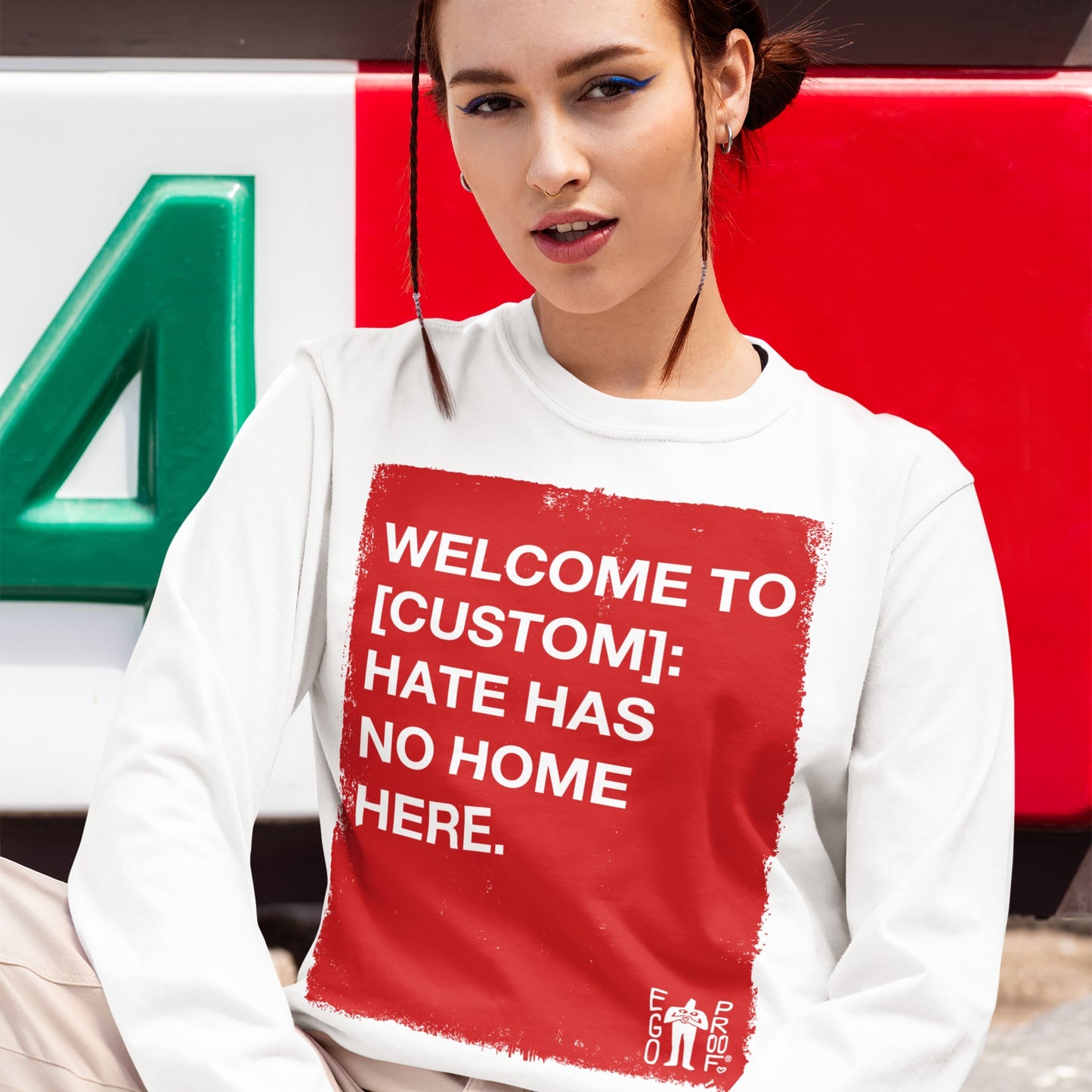 A young person models the Custom Hate Has No Home Here Long Sleeve T-shirt, featuring a bold red square with an anti-hate message, emphasizing community pride and equality.