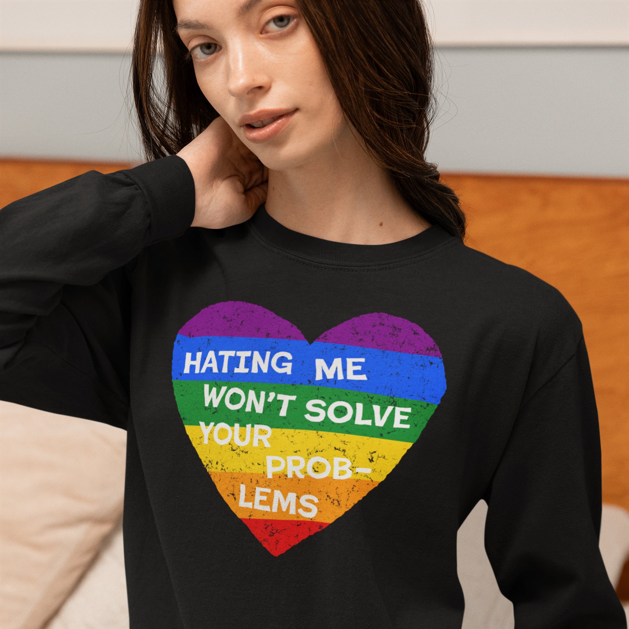 Person wearing the No LGBTQ Hate Shirt: a black sweatshirt with a rainbow-striped heart and bold message, advocating LGBTQ+ love and resistance, against a neutral background featuring a light-colored cushion.