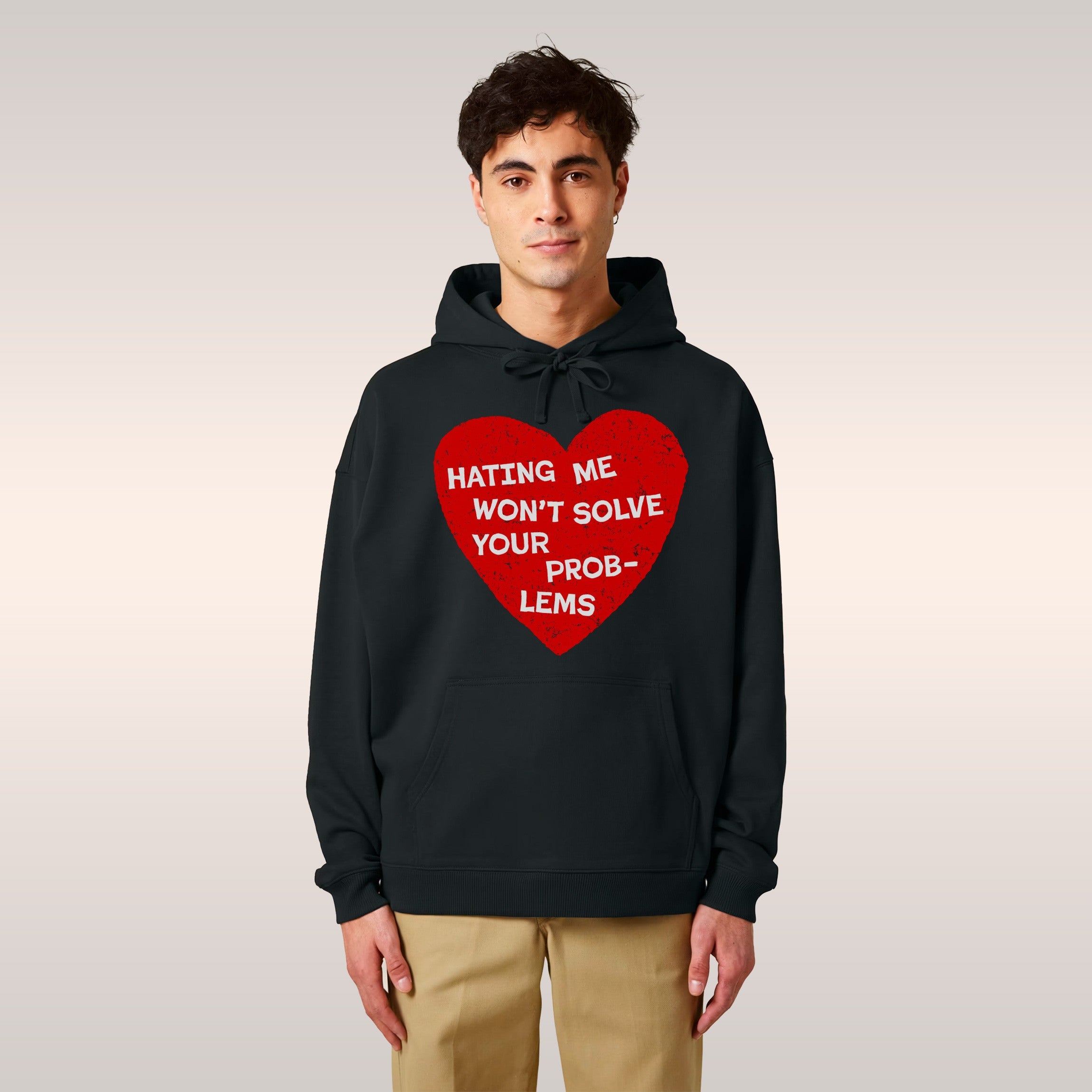 Young man in a cozy café wears the No Hate Shirt, a black hoodie with a bold red heart and the slogan “Hating me won’t s