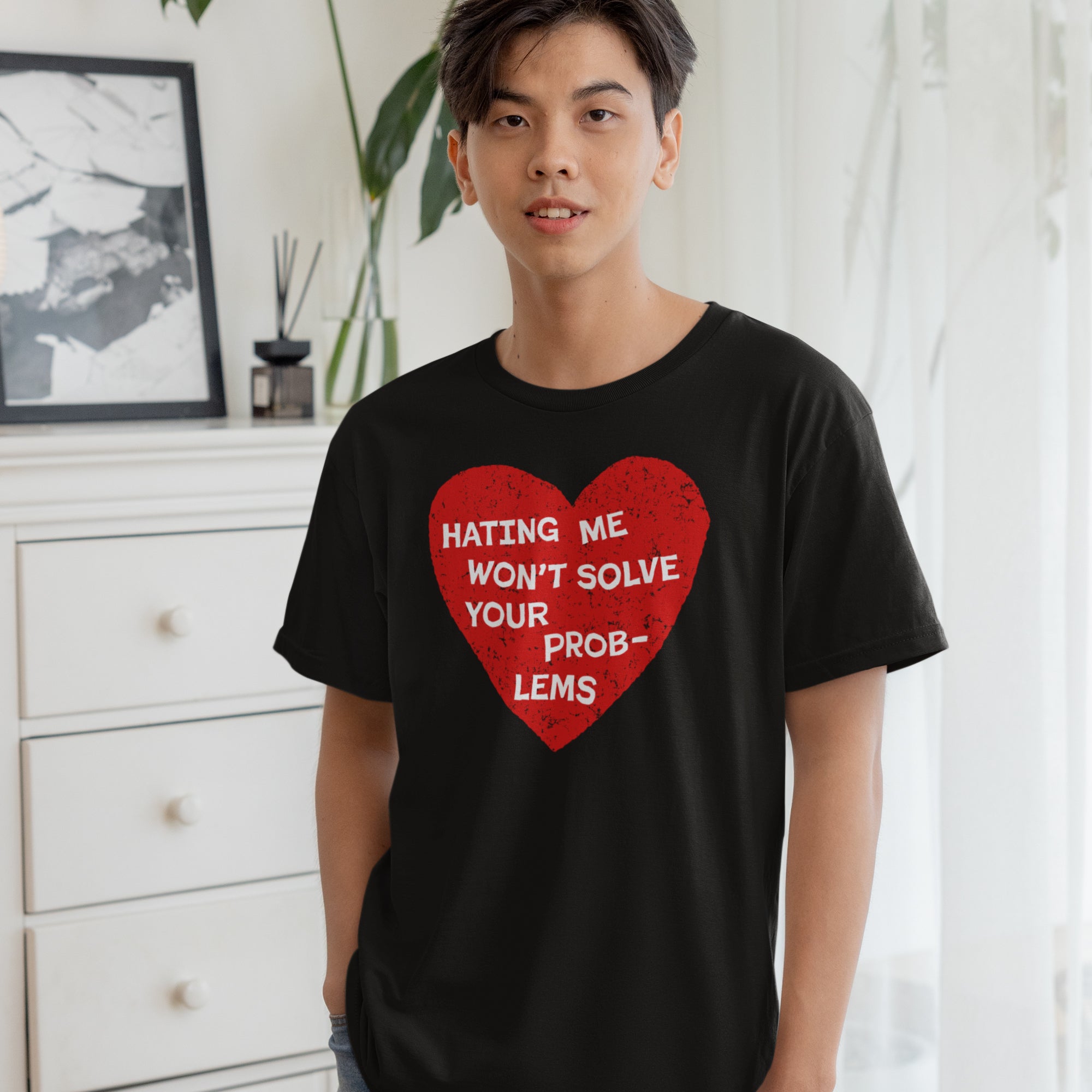 Young man in relaxed indoor setting wears No Hate Shirt featuring a bold red heart with white text: “HATING ME WON’T SOLVE YOUR PROBLEMS.” Promotes love, equality, and supports The Trevor Project.