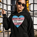 Person in black hoodie with trans flag heart and slogan HATING ME WON’T SOLVE YOUR PROB-LEMS. The No Trans Hate Shirt promotes visibility and pride, supporting The Trevor Project.