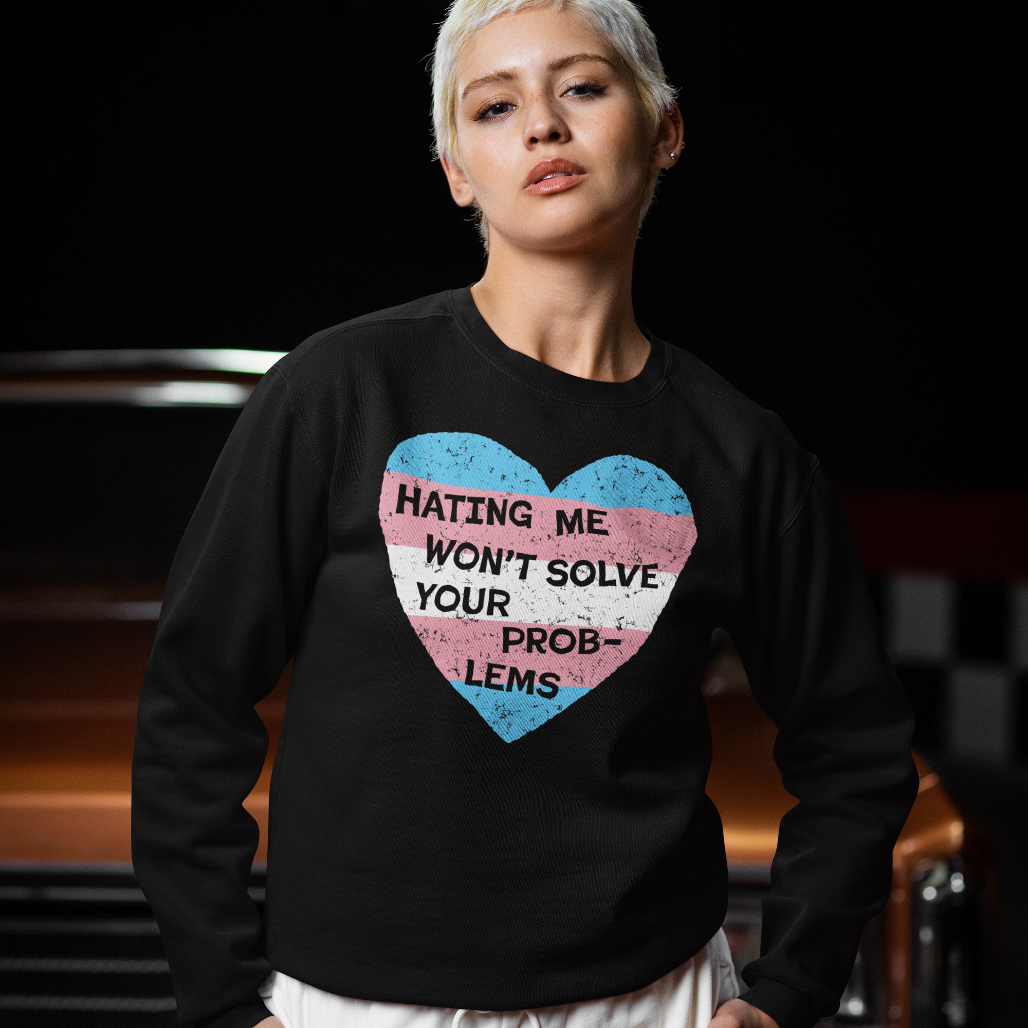 A person wears a black No Trans Hate Shirt featuring a distressed heart with trans flag colors and the slogan HATING ME WON'T SOLVE YOUR PROBLEMS in vibrant support of trans pride.