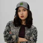 Young woman wearing the Hop Nug Hat, a gray-and-black baseball cap with a green hop-cone graphic. Her bomber jacket with botanical motifs complements her casual, confident style.