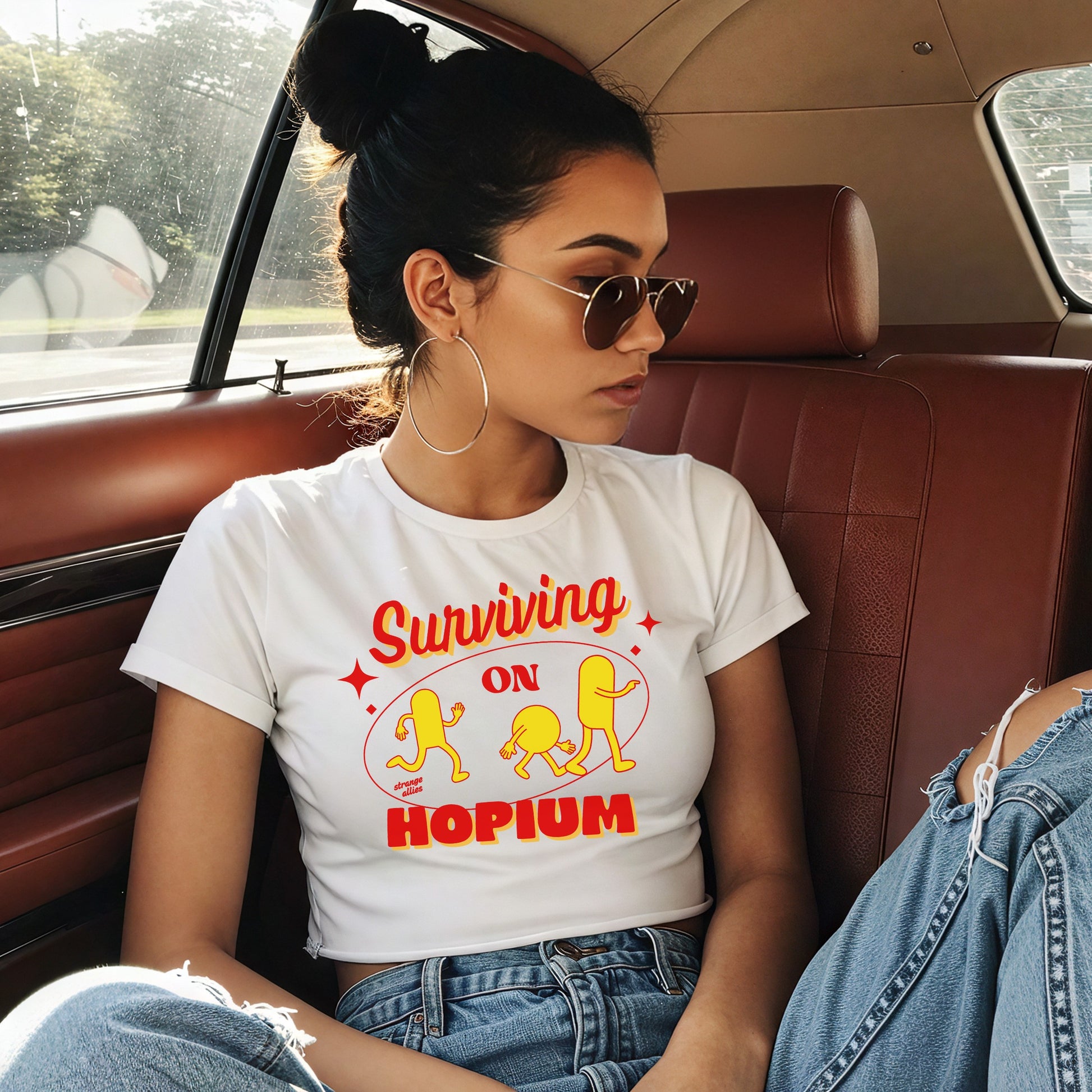 Young woman in a car wearing the Hopium Women's Baby Tee with retro lettering and cartoon pill figures, paired with aviator sunglasses and ripped jeans, embodying a carefree, rebellious spirit.