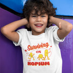 Young child smiling, wearing a white Hopium Shirt with retro pill-shaped characters and Surviving on Hopium text, embodying playful optimism and individuality.