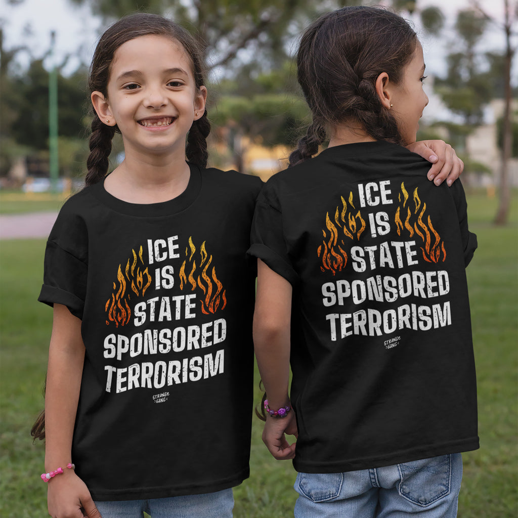 Two girls in a park wear the ICE Is State Sponsored Terrorism black T-shirts, featuring orange flames and bold white text, symbolizing a stance for immigrant rights and activism.