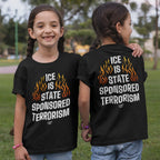 Two girls in a park wear the ICE Is State Sponsored Terrorism black T-shirts, featuring orange flames and bold white text, symbolizing a stance for immigrant rights and activism.