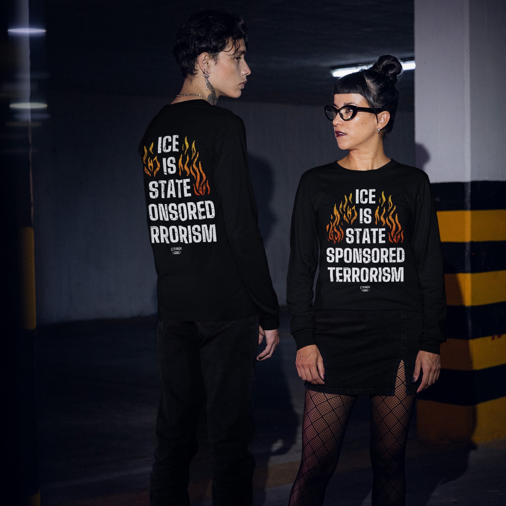 Two people wear the ICE Is State Sponsored Terrorism T-shirt featuring bold flaming designs and protest text, showcased front and back in a dimly lit parking garage.